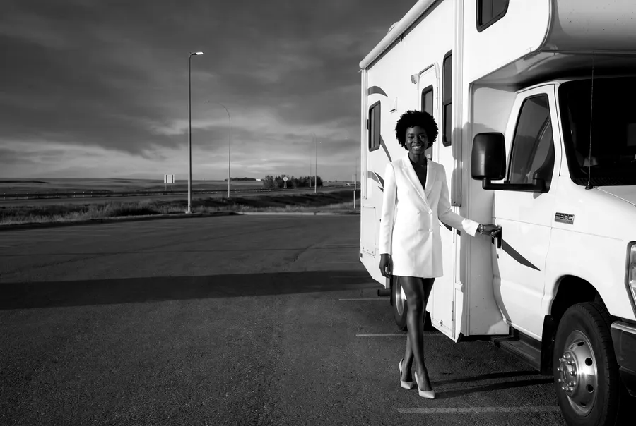 Black-and-white generated image: the guide's character stands by a white motorhome on a wide paved lot at dusk.